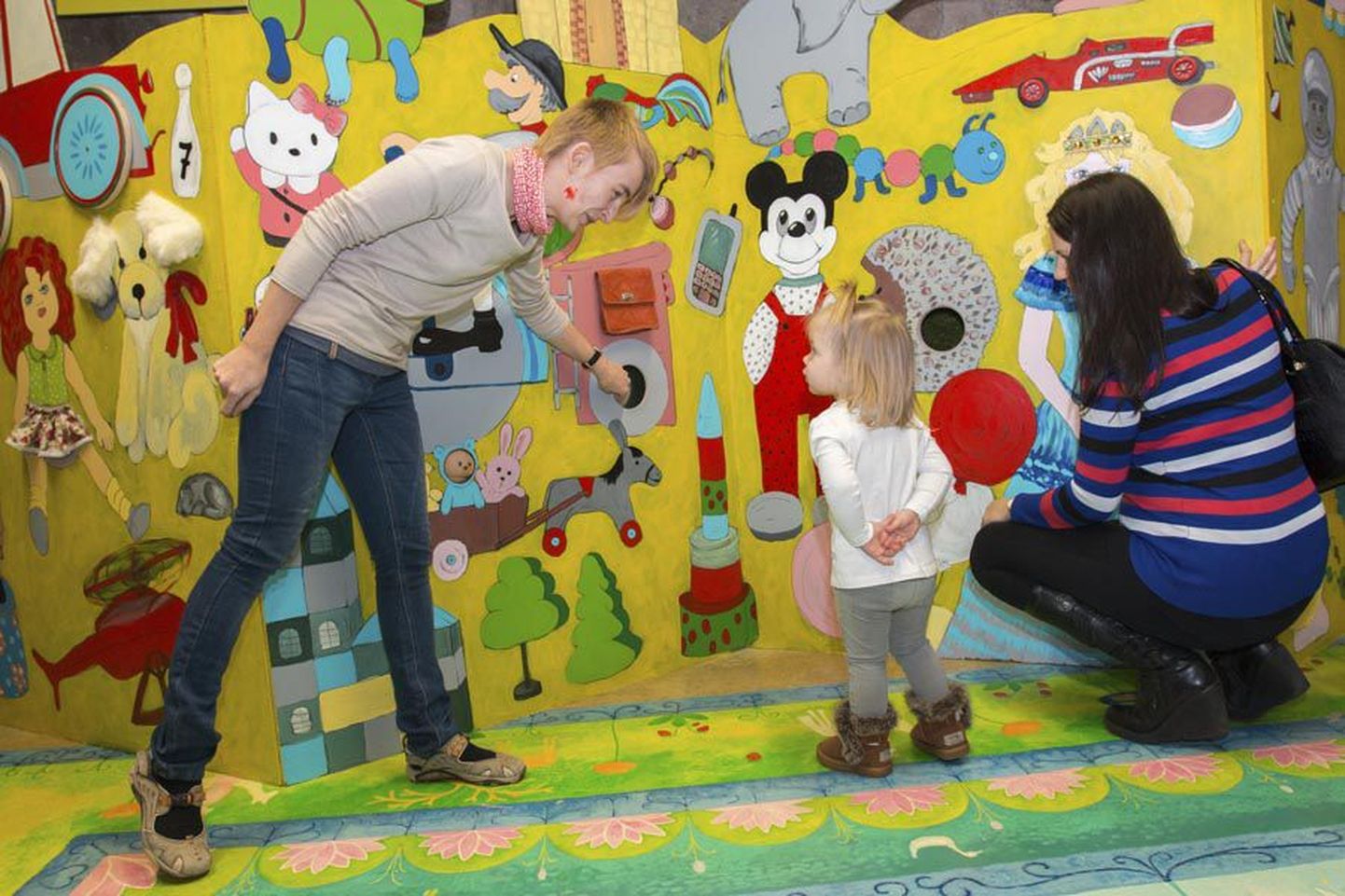 Väike Isabel uurib koos ema (paremal) Merlin Jänese ja mänguasjamuuseumi töötaja Marge Pärnitsaga, mis põnevad asjad on seina taga varjul.