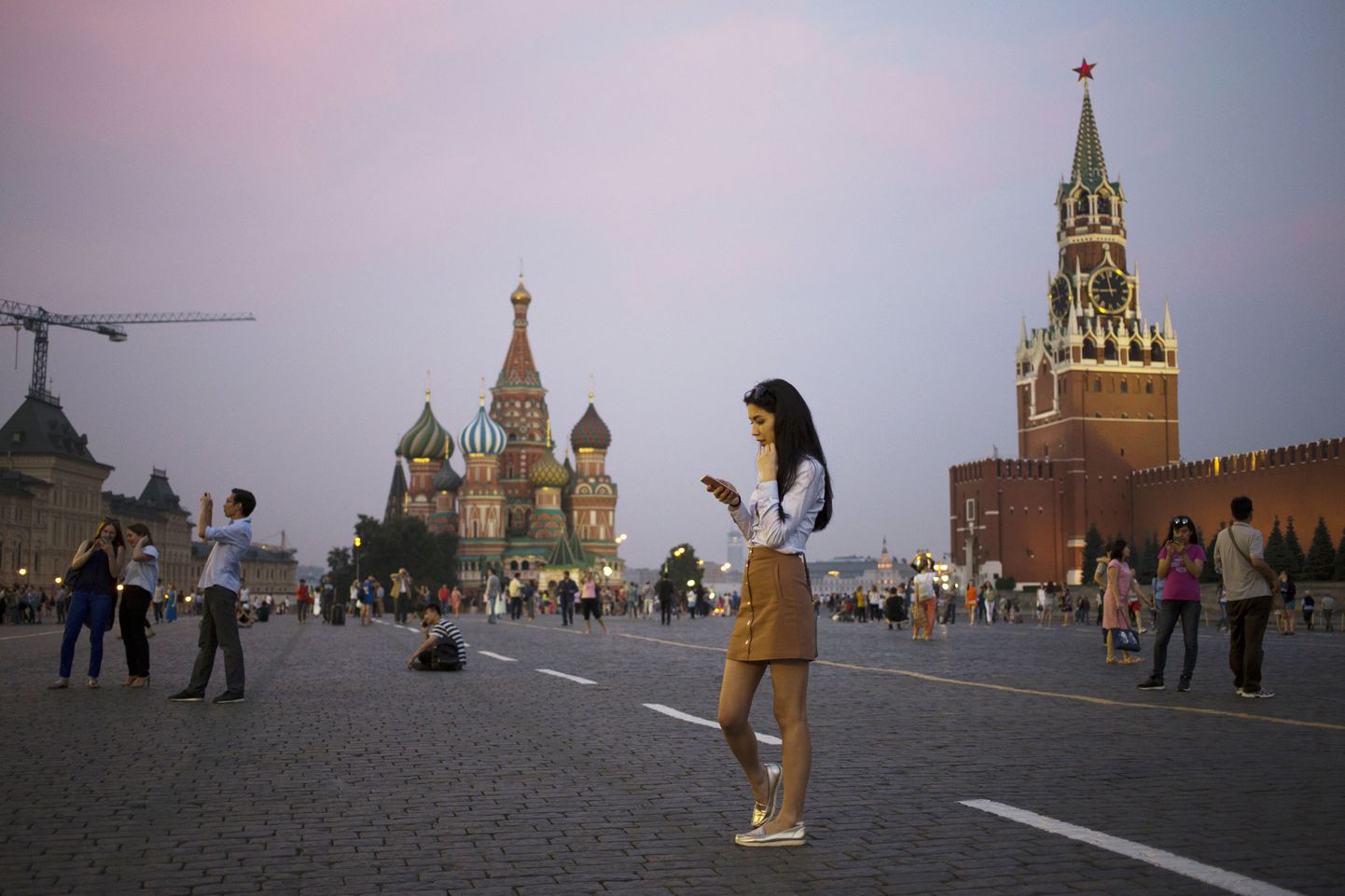 A young woman holds her smartphone at Red Square with the Kremlin's Spasskaya Tower, right, and St. Basil Cathedral, center, in the background in Moscow, Russia, Monday, July 25, 2016. (AP Photo/Pavel Golovkin)