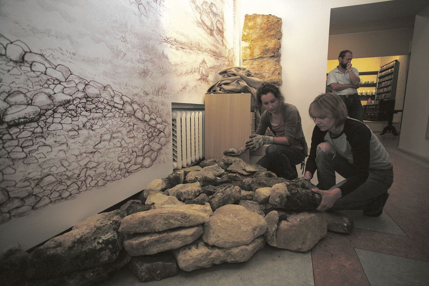 Arheoloogid Mari Lõhmus (ees vasakul) ja Kristiina Johanson sätivad mündi karjäärist toodud paekive seinajoonistuselt ruumi jätkuvasse tarandkalmesse.