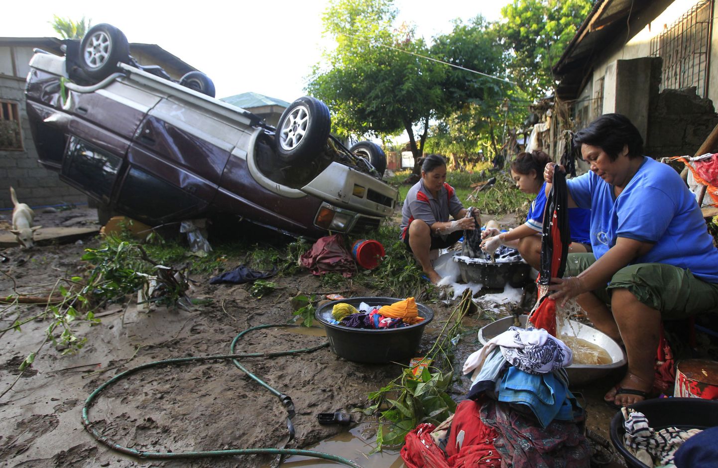 Cagayan de Oro elanikud pesemas pesu, kõrval taifuun Washi tõttu kummuli paiskunud auto.