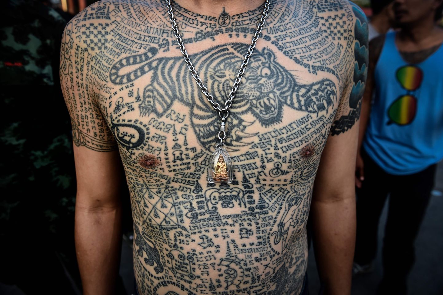 A devotee wears a Buddhist amulet over his tradtional tattoos during an annual sacred tattoo festival, at the Wat Bang Phra temple in Nakhon Chaisi district, Thailand's Nakhon Pathom Province, on March 3, 2018. 
Ever year, thousands of Buddhist devotees gather at Thailand's Wat Bang Phra temple for an annual festival celebrating traditional Sak Yant tattoos, which wearers believe will bring them good luck and protection from harm. / AFP PHOTO / LILLIAN SUWANRUMPHA