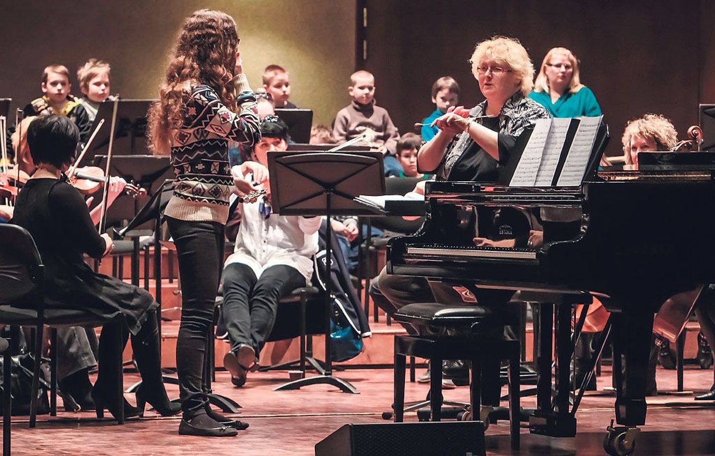 Solist Jennie Ry Lootus kuulab dirigent Lilyan Kaivi õpetussõnu, taamal jälgivad proovi koolilapsed.