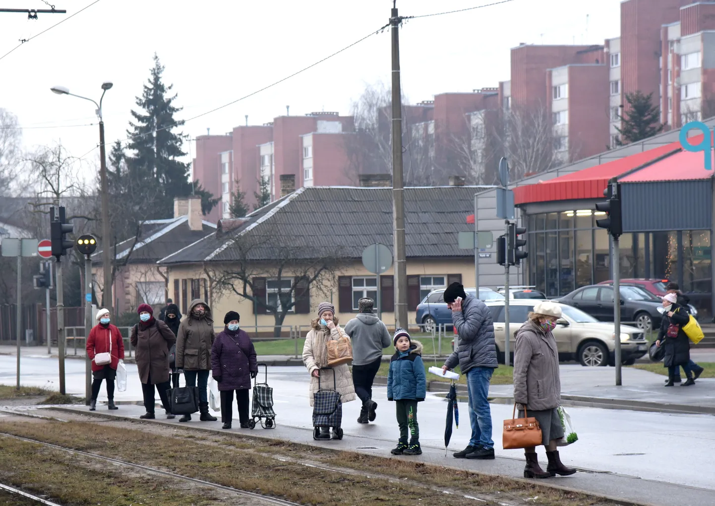 Cilvēki sejas maskās sabiedriskā transporta pieturvietā Covid-19 pandēmijas laikā.