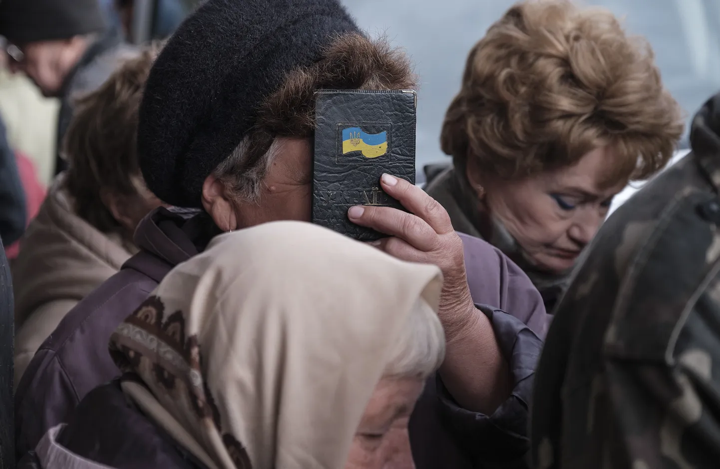 Ida-Ukrainas peidab eakas naine pensionijärjekorras oma näo Ukraina lipu kleepsuga passi taha 5. oktoobril 2022