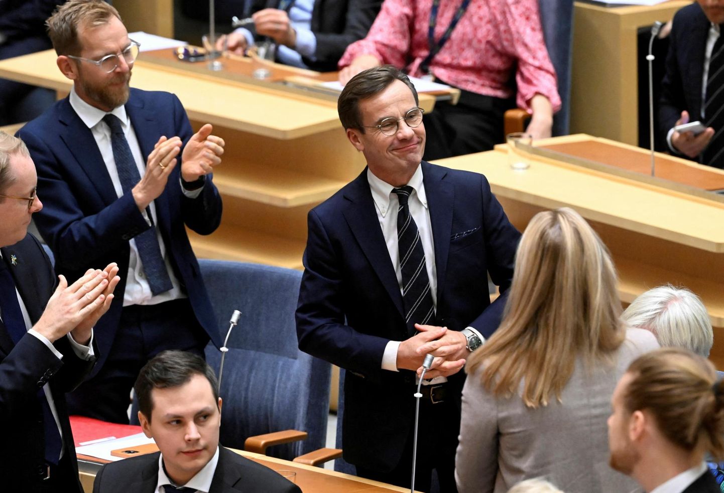 Rootsi peaministriks valitud Moderaatide esimees Ulf Kristersson (keskel) võtab eile parlamendi istungisaalis vastu õnnitlusi.