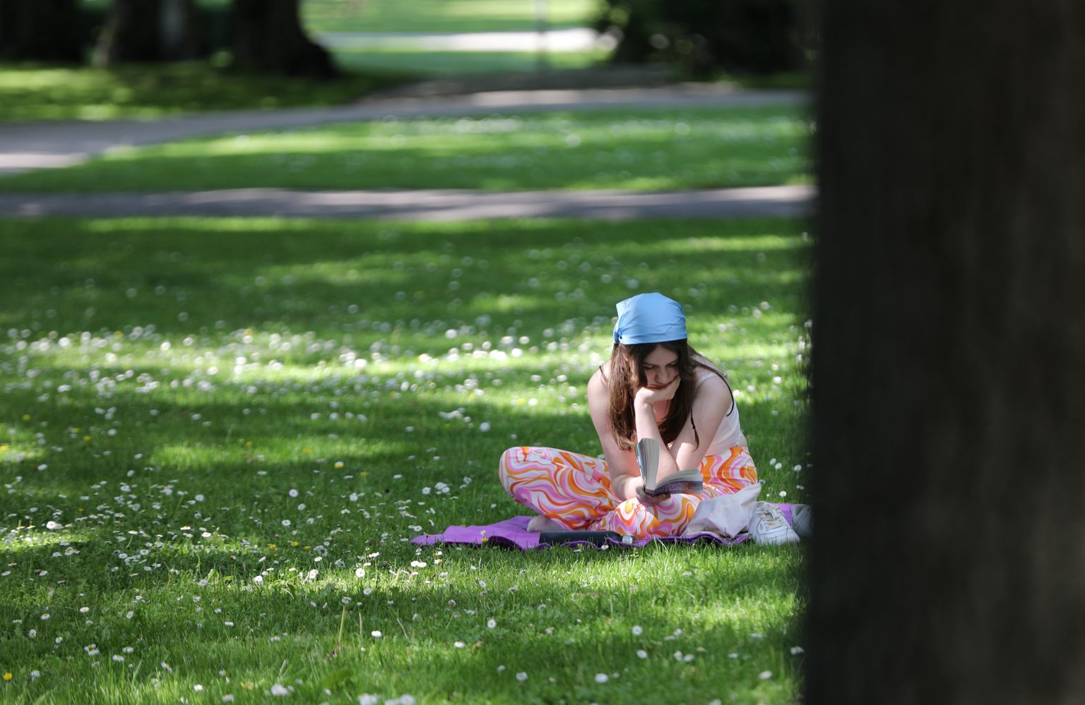 Meitene lasa grāmatu zālienā Kronvalda parkā.
