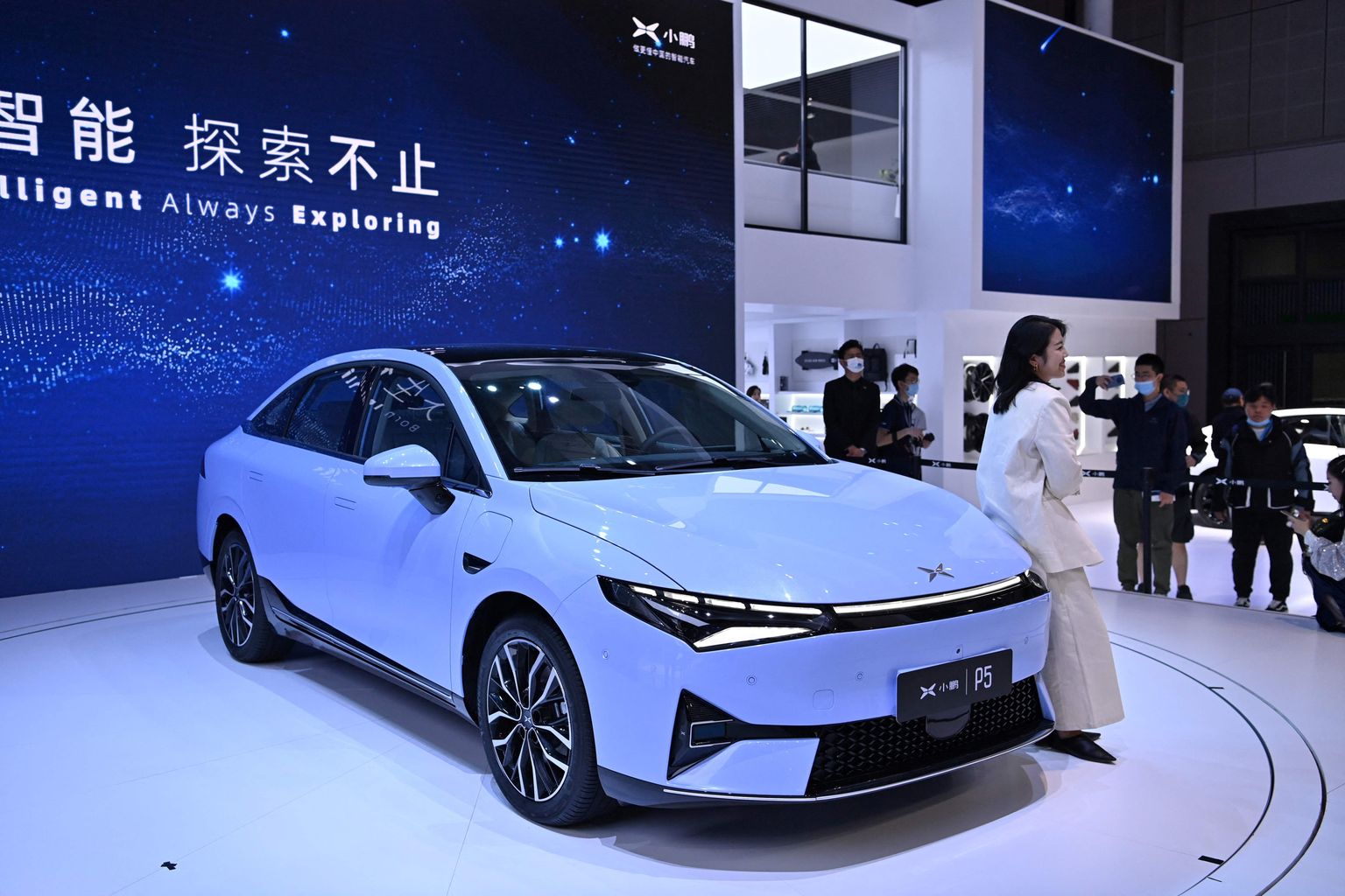 Heledais rõivais hiinlanna nõjatumas elektriautole Xpeng P5 Shanghai 19. rahvusvahelisel autonäitusel 19. aprillil 2021. Masin mõtleb maanteedele kõikjal laias maailmas.