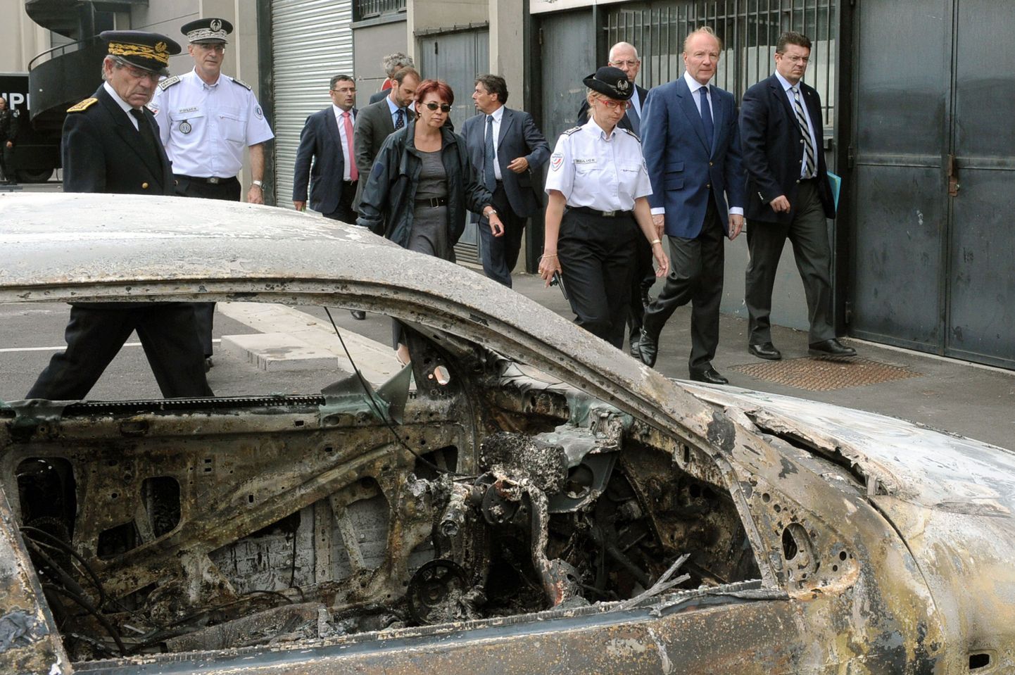 Prantsuse siseminister Brice Hortefeux (paremalt teine) kõndimas mööda rahutuste käigus süüdatud autost.