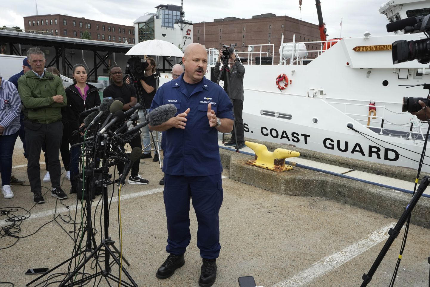 U.S. Coast Guard Capt. Jamie Frederick, center, faces reporters during a news conference, Tuesday, June 20, 2023, at Coast Guard Base Boston, in Boston. The U.S. Coast Guard says a search covering 10,000 square miles (26,000 square kilometers) has turned up no signs of a missing submersible off New England. Authorities made the announcement Tuesday. (AP Photo/Steven Senne)  MASR105