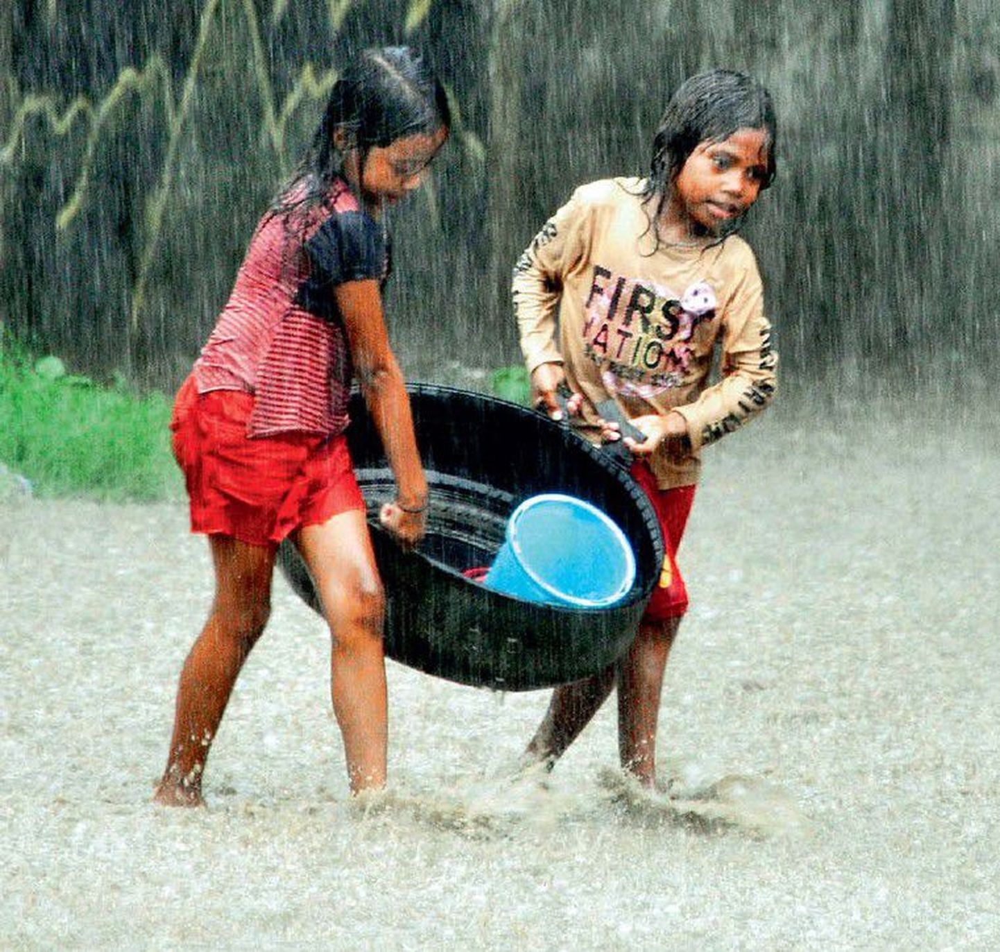 Kaks Ida-Timori tüdrukut tassivad majakraami läbi tiheda vihmasaju.