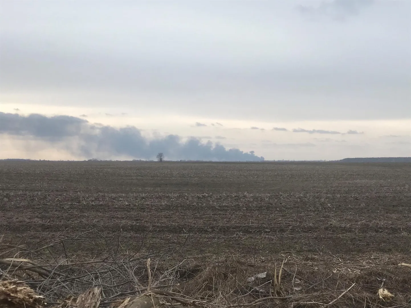 Üles küntud põllumaa Ukrainas, taamal on näha Tšernihivi linna pommitamise tagajärjel tekkinud põlengut.