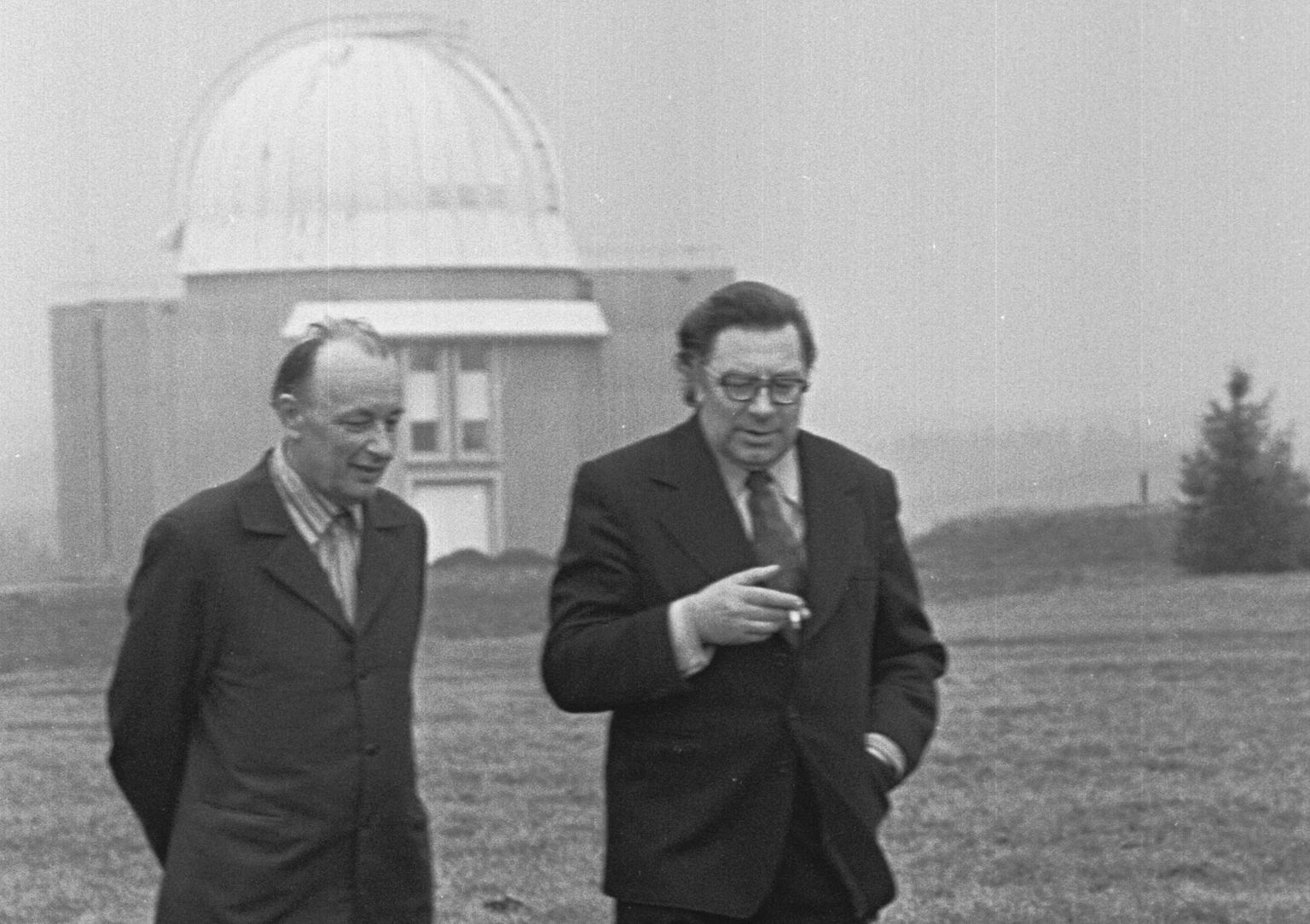 Tõravere observatoorium. Professorid Grigori Kuzmin ja Charles Villmann jalutavad midagi arutades mööda teed. Tagaplaanil üks Tõravere observatooriumi kuplitest. Grigori Kuzmin (1917-1988) oli Ernst Öpiku õpilane ja Jaan Einasto õpoetaja.