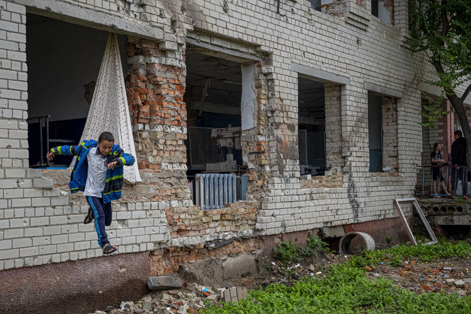 Ребенок выпрыгивает из окна своей сильно поврежденной школы в селе Олизаровка, Украина, 13 августа 2022 года. Деревня пережила ожесточенные бои на ранних этапах эскалации войны.