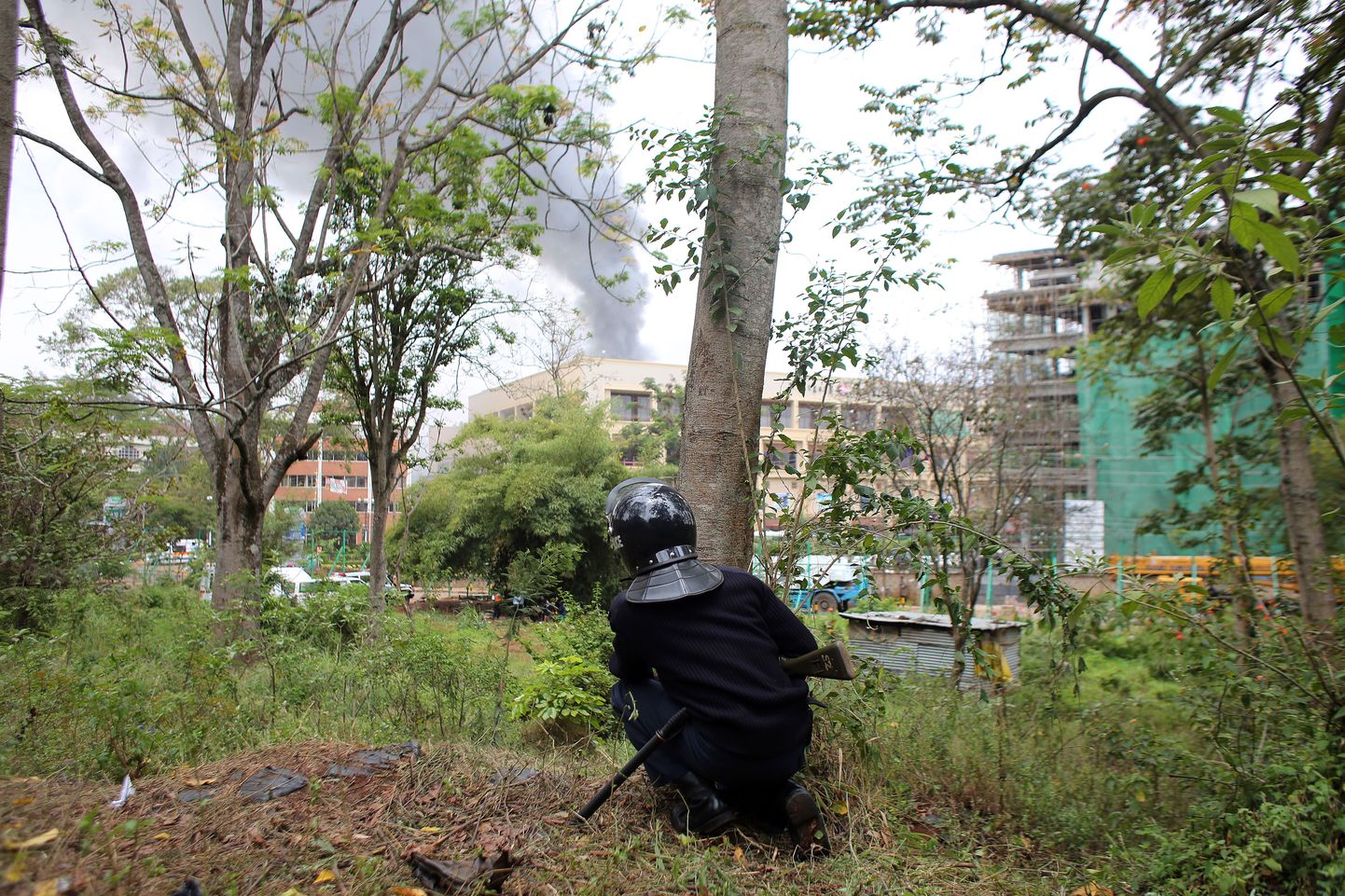 Kenya politseinik jälgib põlevat Westgate'i ostukeskust puu tagant.