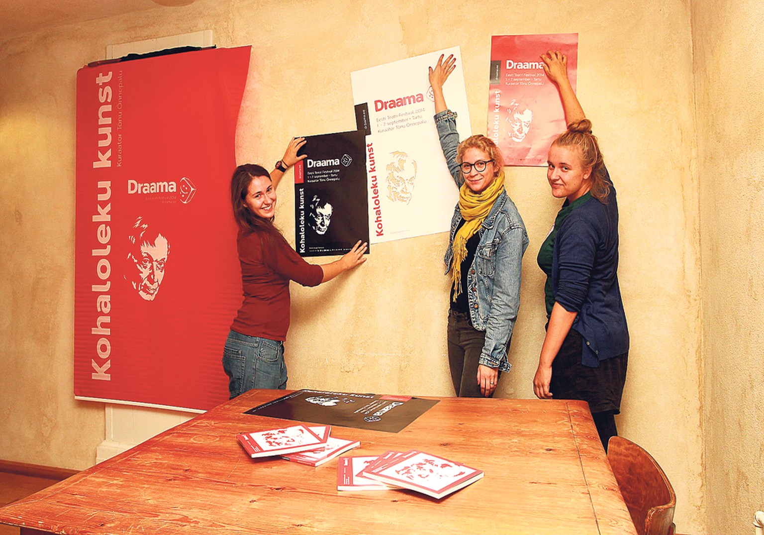 Festivali kunstnikud Katarina Klett (vasakult) ja Annika Lindemann ning festivali tegevjuht Kadi Rutens näitavad Draama plakateid, millest osa on juba linna üles pandud. Laual on eile trükist tulnud festivaliraamatud.