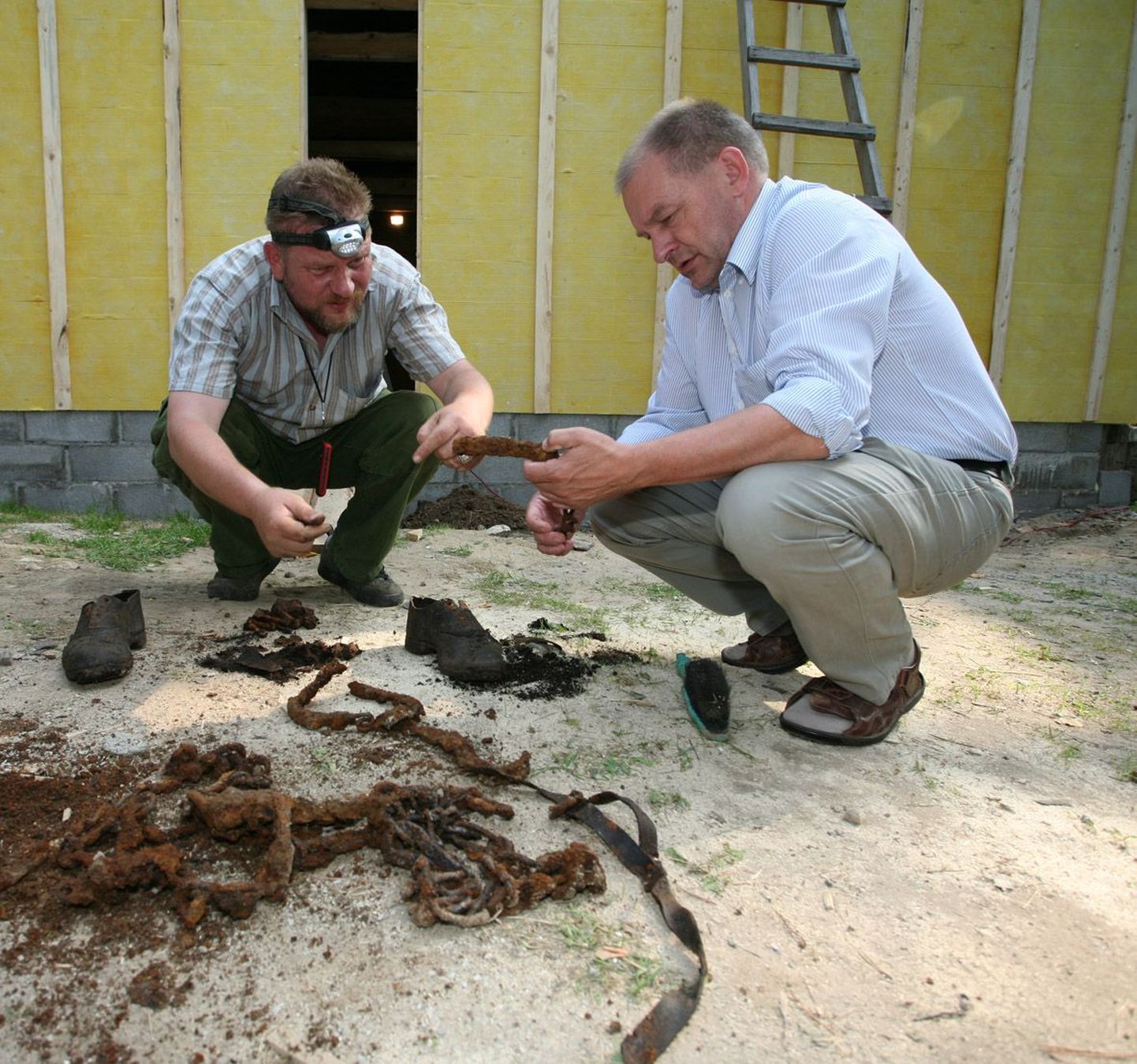 Sõjahaudade uurija Arnold Unt (vasakul) ja muinsuskaitseameti peainspektor Ants Kraut uurivad maja alla maetud skeleti juurest leitud jalanõusid, nahkrihma ja lehmaketti.
