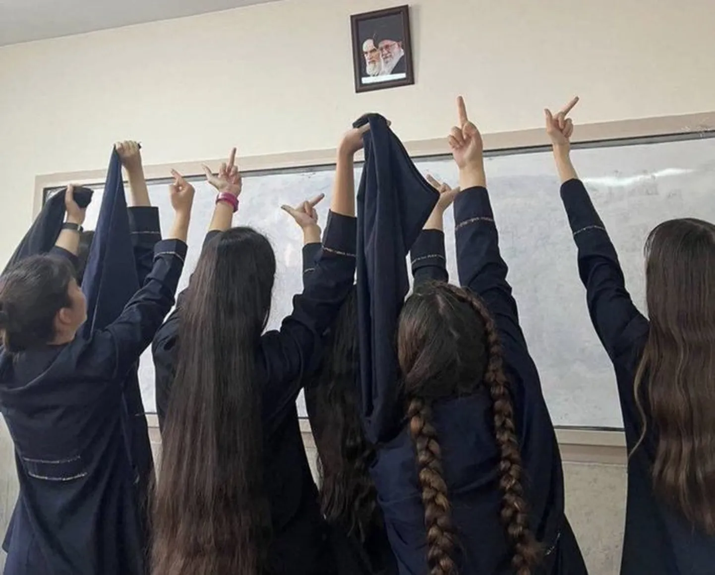 Иранские девочки, сняв хиджабы, показывают средний палец фотографии президента Али Хаменеи, одному из ближайших соратников лидера Исламской революции.