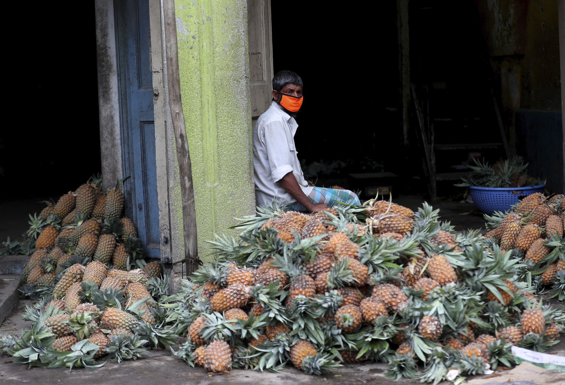 Maskis ananassikaupmees ootab Indias Bengaluru puuvilja hulgimüügiturul ananassikuhja kõrval ostjaid (30. mail 2020). India leevendas maikuus riigis kehtinud koroonapiiranguid; avati taas müügikohad, jätkus rongiliikus ja siselennud. Sellest alates on nakkusjuhtumite arv pidevalt tõusnud. 20. septembril lisandus ligi 94 000 uut nakatunut; samas suurusjärgus on lisandunud nakatunuid iga päev viimase kahe nädala jooksul.