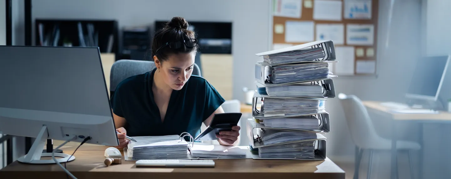 Young Businesswoman Working At Office With Stack Of Folders On Desk