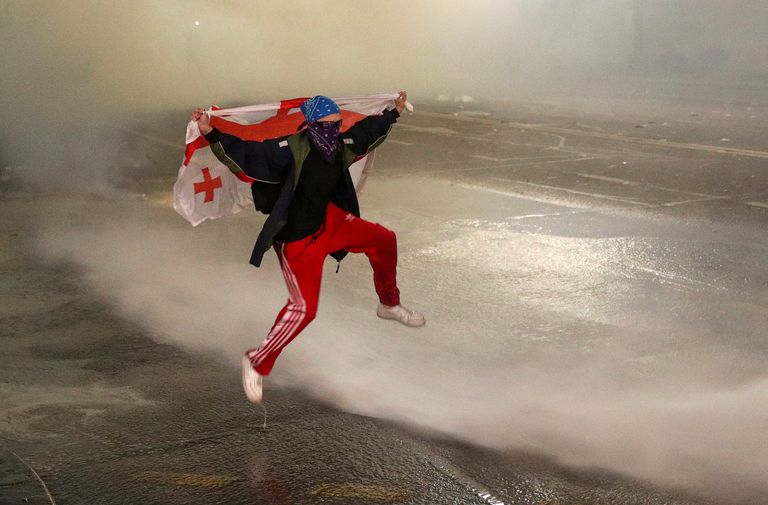Протестующий перепрыгивает через струю полицейского водомета на стихийном митинге в Тбилиси против законопроекта об «иностранных агентах», который, по мнению критиков, ведет к авторитаризму и вредит стремлению Грузии к вступлению в Европейский союз. 9 марта 2023 года.