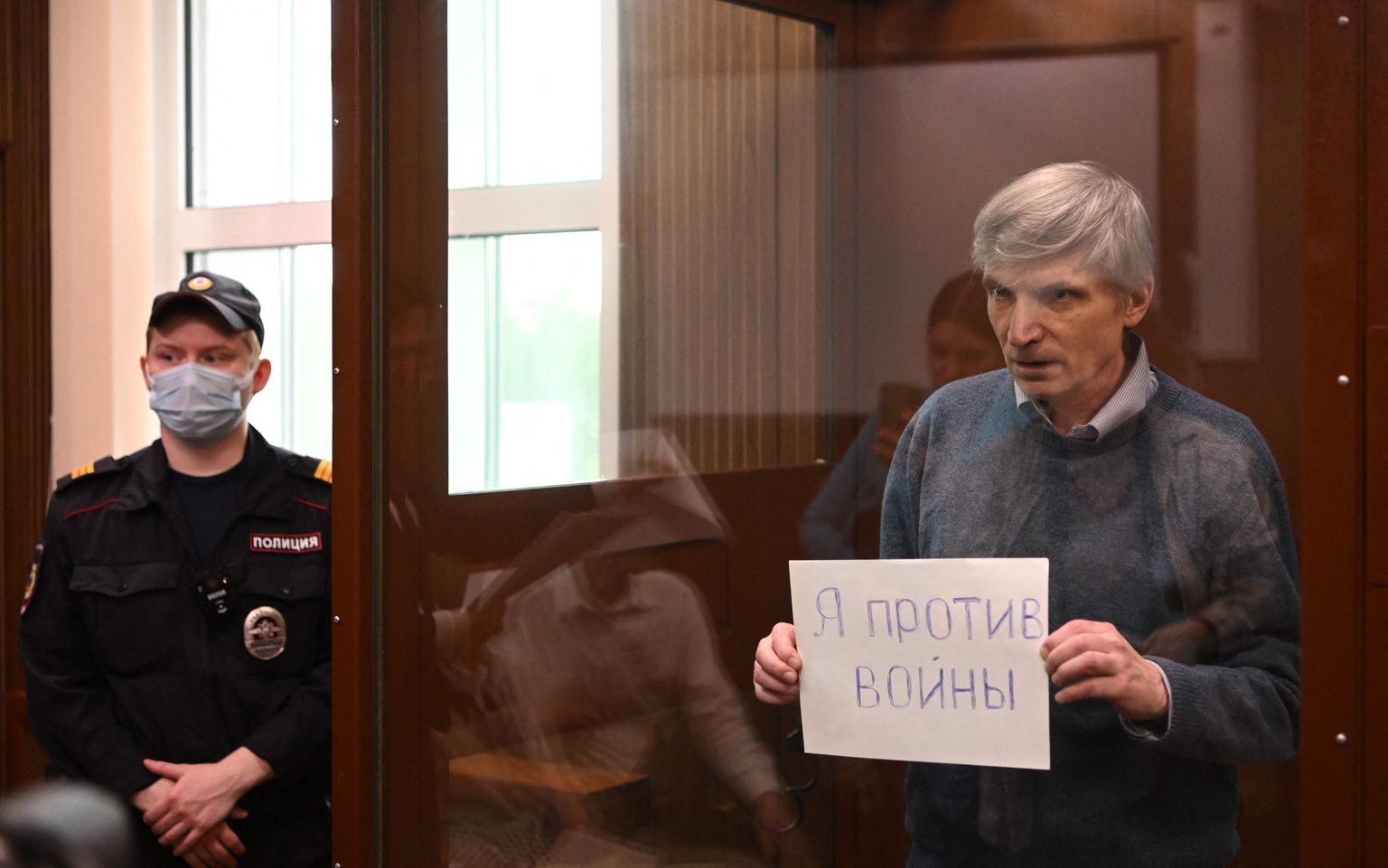 Депутат Алексей Горинов держит лист бумаги с надписью «Я против войны» в стеклянной камере во время судебного заседани, 21 июня 2022 года