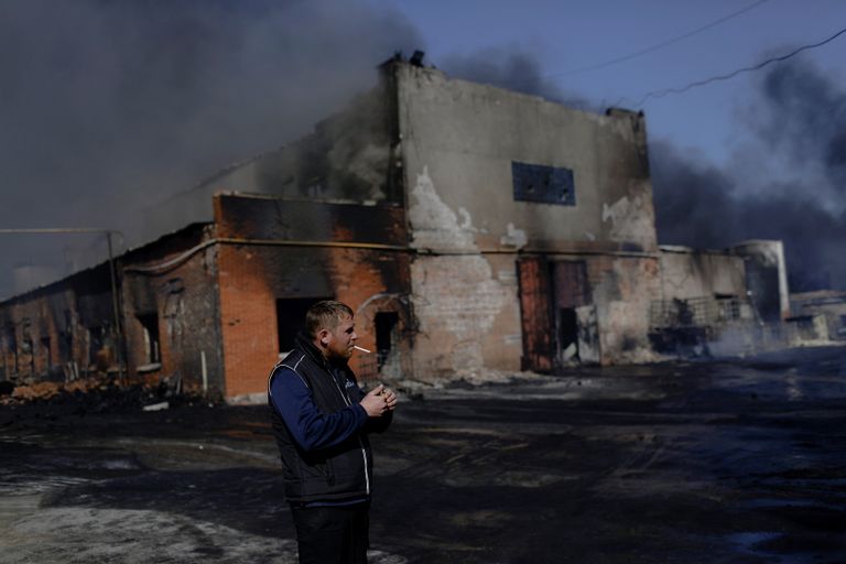 Mees suitsetamas Harkivis eile tabamuse saanud põleva tehase ees.