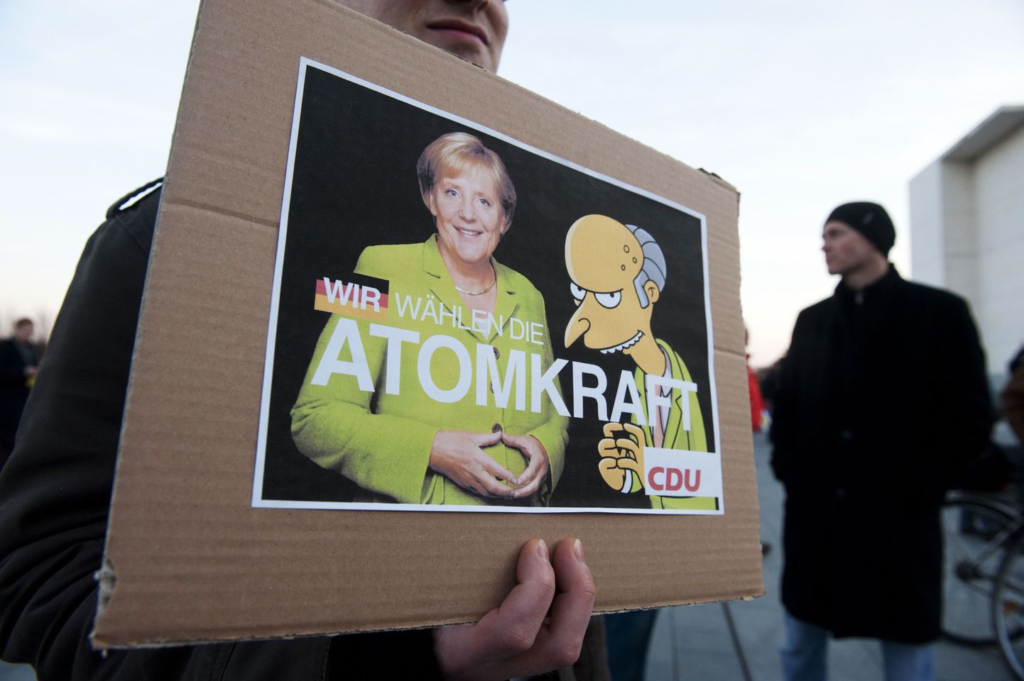Tuumaenergia-vastane meeleavaldaja Berliinis plakatiga, millel Saksamaa kantsler Angela Merkel ja Springfieldi tuumajaama omanik Montgomery Burns kuulutavad: "Me valime tuumaenergia".