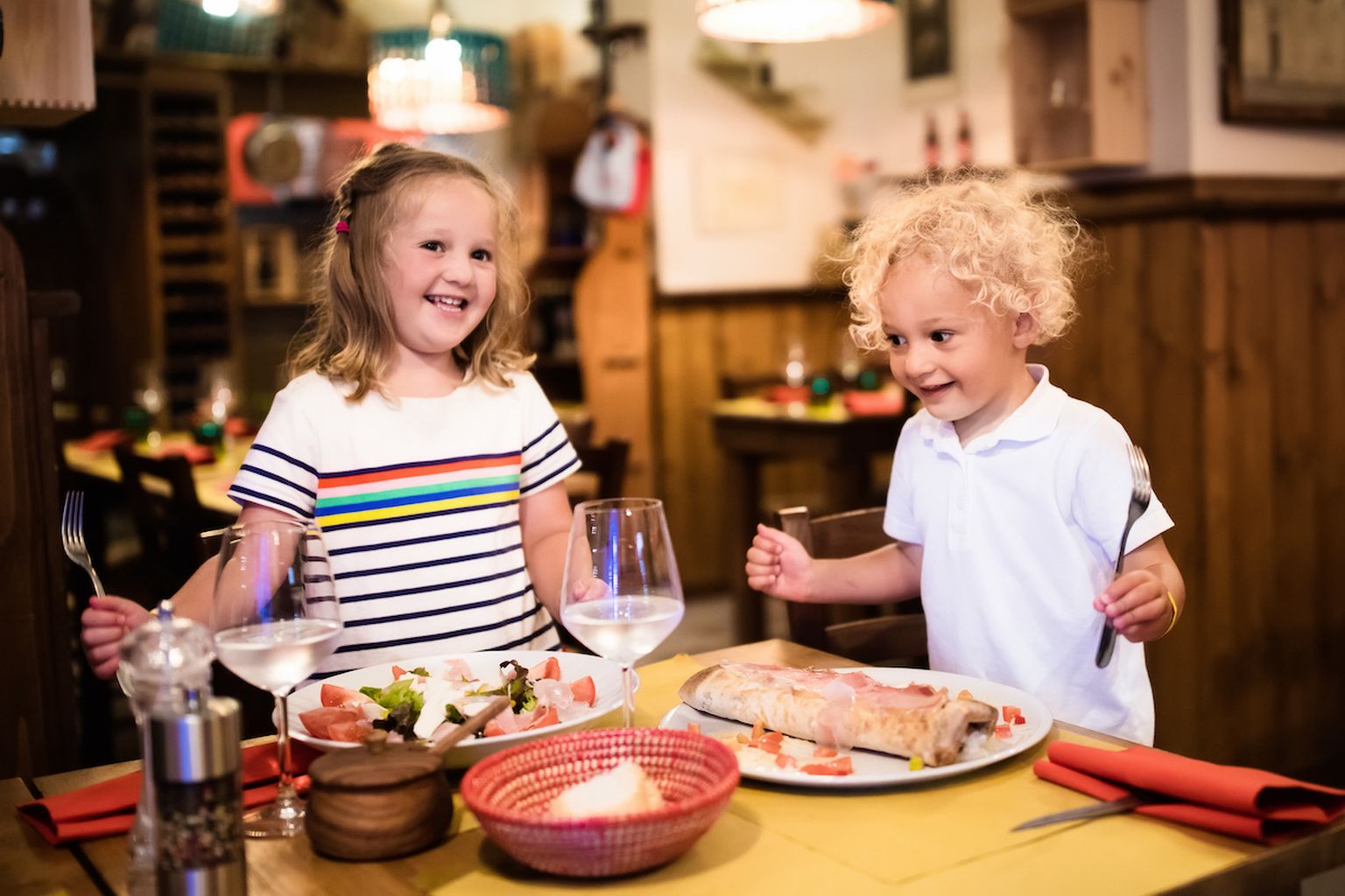 Kids eat pizza, pasta and salad in traditional restaurant.  Eating out with children. Boy and girl having dinner in pizzeria in Italy on vacation in Europe. Italian food and cuisine for family.