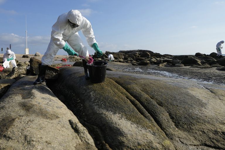 Workers scrubbing oil off rocks on Mae Ramphueng Beach after a pipeline oil spill off the coast of Rayong province in eastern Thailand, Sunday, Jan. 30, 2022. Favorable wind and sea conditions kept an oil slick away from beaches in eastern Thailand on Sunday, according to authorities, but concerns remained that the spillage may yet strike a popular resort island. (AP Photo/Sakchai Lalit)