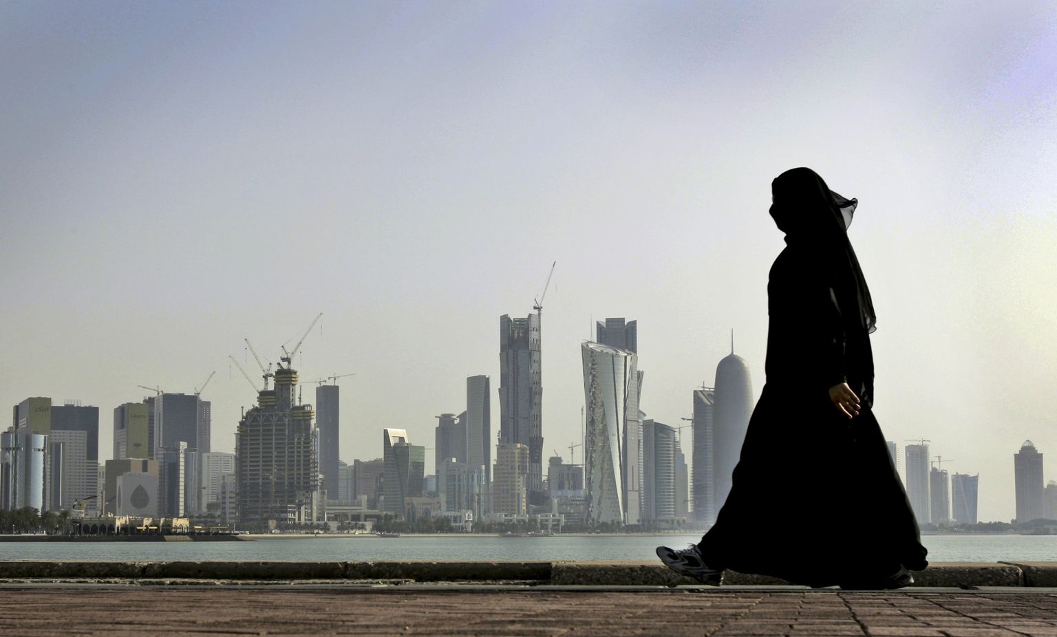 Qatari naine kõnnib Doha linnapildi ees.