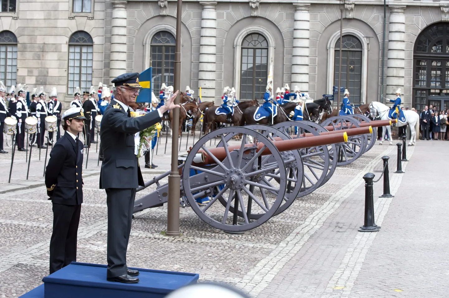 Sünnipäevalaps Carl XVI Gustaf tervitab rootslasi kuningalossi juures Stockholmis. Riigipea kõrval seisab tema poeg prints Carl Philip.