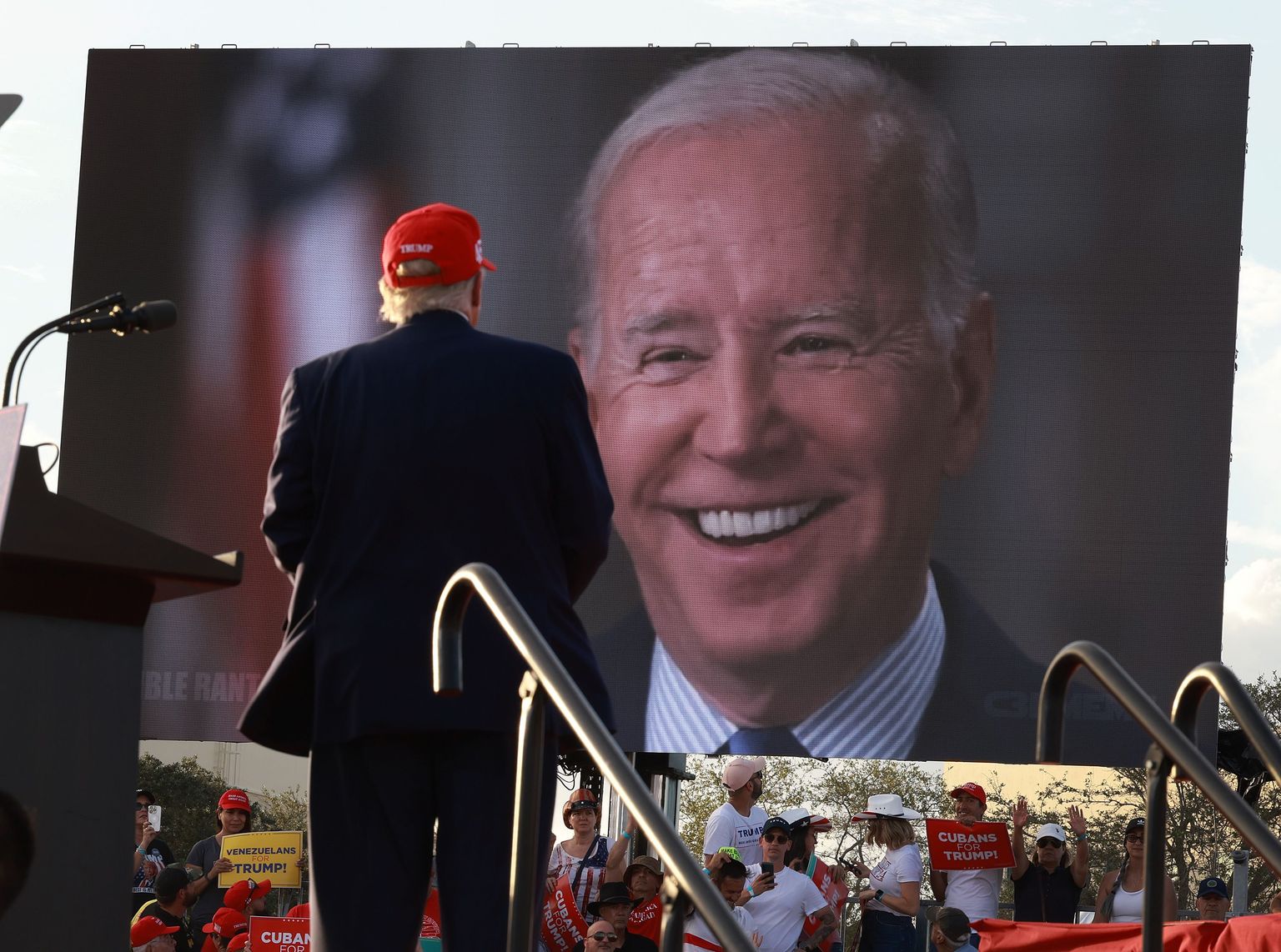 Endine USA president Donald Trump (punamütsis) pidamas vahevalimiste kampaaniakoosolekut praeguse presidendi Joe Bideni video taustal Miamis 6. novembril 2022.