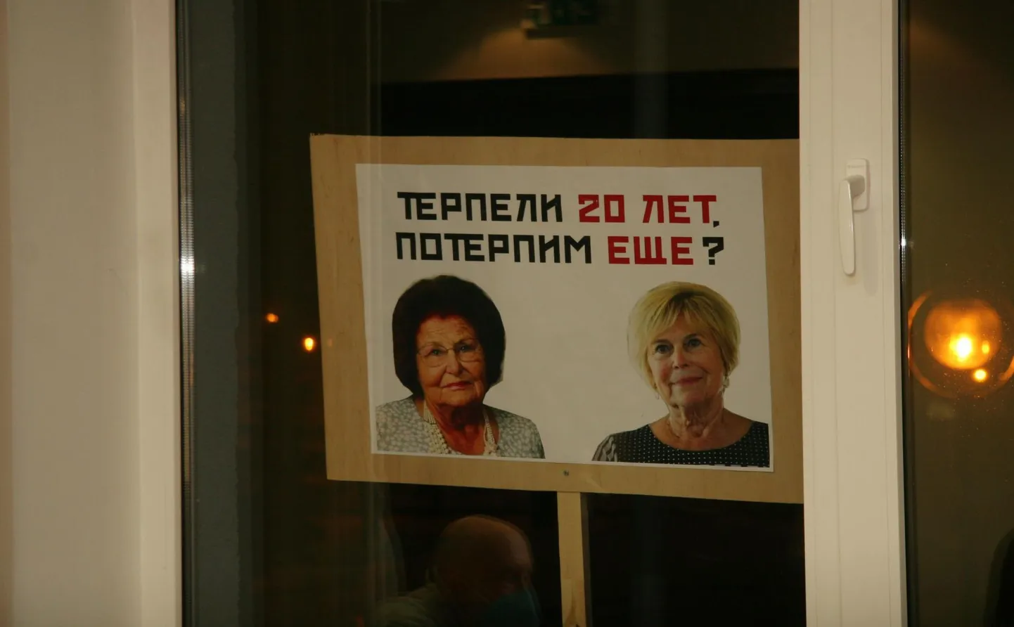 Meeleavaldajate plakat Kohtla-Järve volikogu istungil akende taga. Karikatuuril on kujutatud hiigelhüvitisi saavaid abilinnapeasid Ljudmila Jantšenkot ja Riina Ivanovat. «Kannatasime 20 aastat, kas kannatame veel?» küsis plakat.