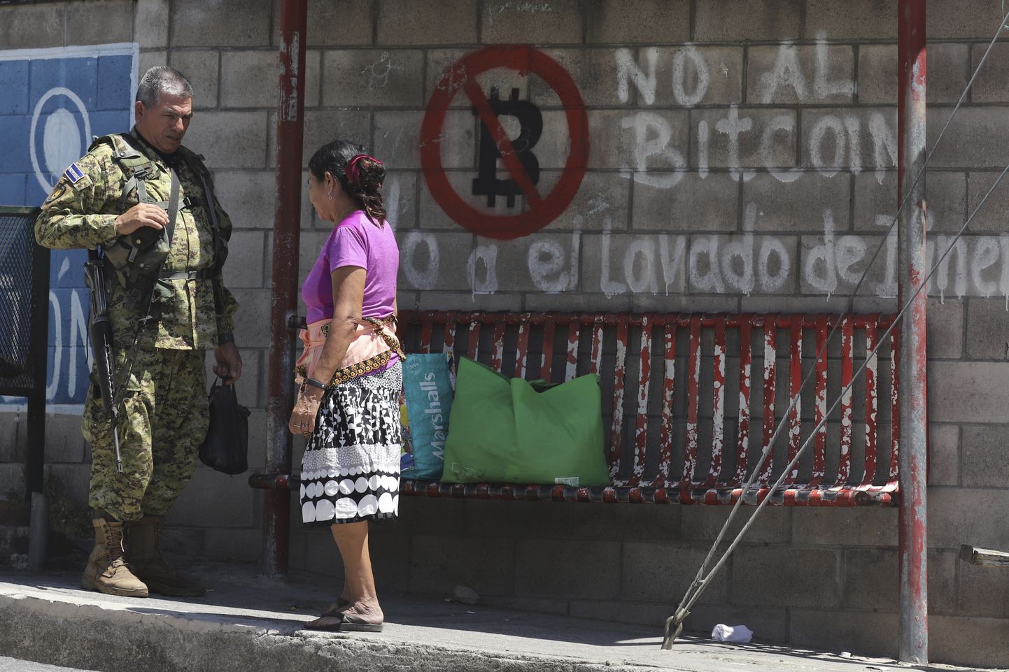 Sõdur räägib San Jose Las Florese bussipeatuses kohaliku elanikuga. Taustal on enne valimisi tekkinud grafiti, mis lükkab tagasi bitcoin'i.