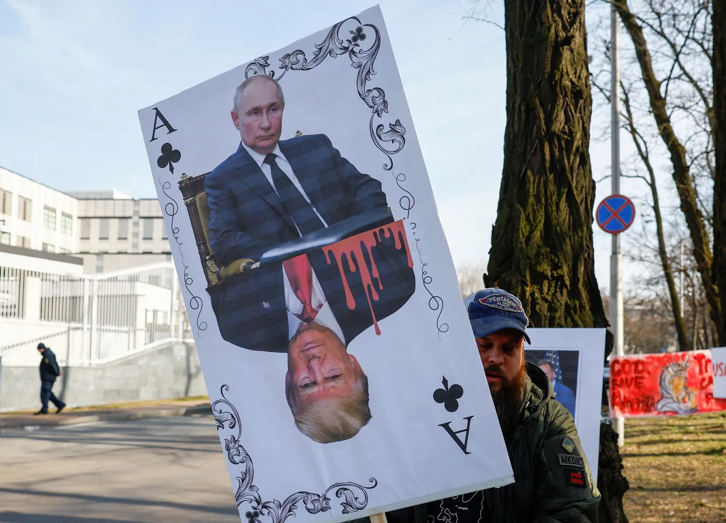 Протестующий держит плакат с игральной картой, на которой изображены президент США Дональд Трамп и президент России Владимир Путин.