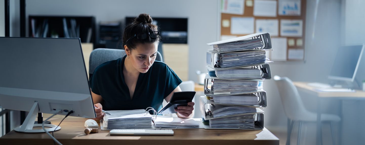 Young Businesswoman Working At Office With Stack Of Folders On Desk