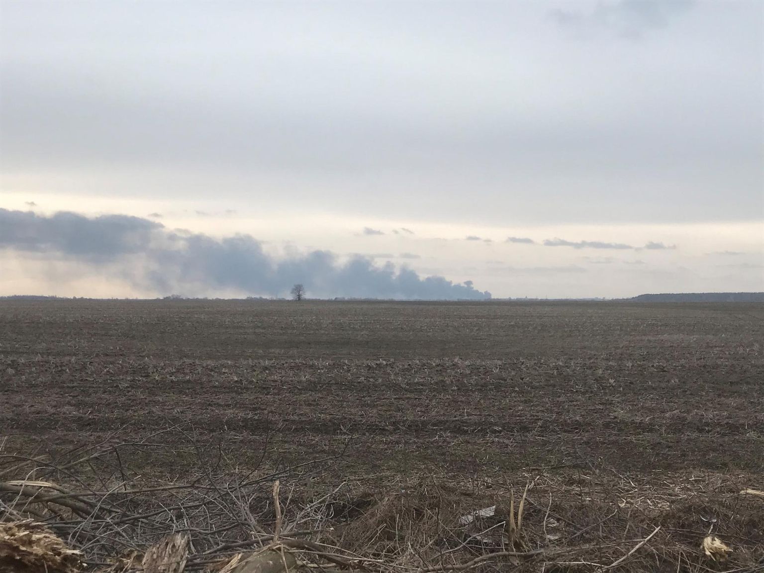 Üles küntud põllumaa Ukrainas, taamal on näha Tšernihivi linna pommitamise tagajärjel tekkinud põlengut.