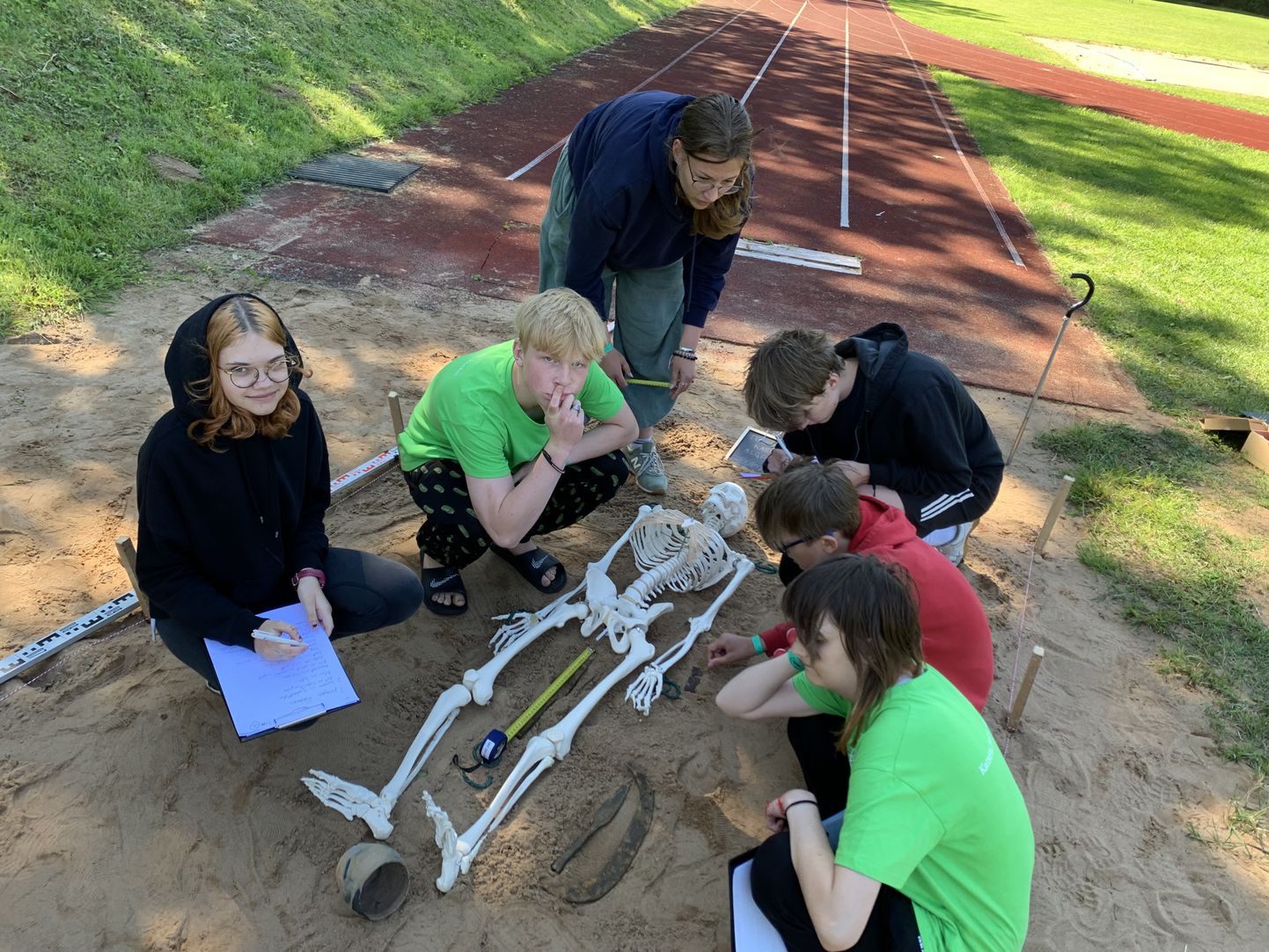 Участники лагеря в секторе для прыжков изучают в ящике с песком скелет.