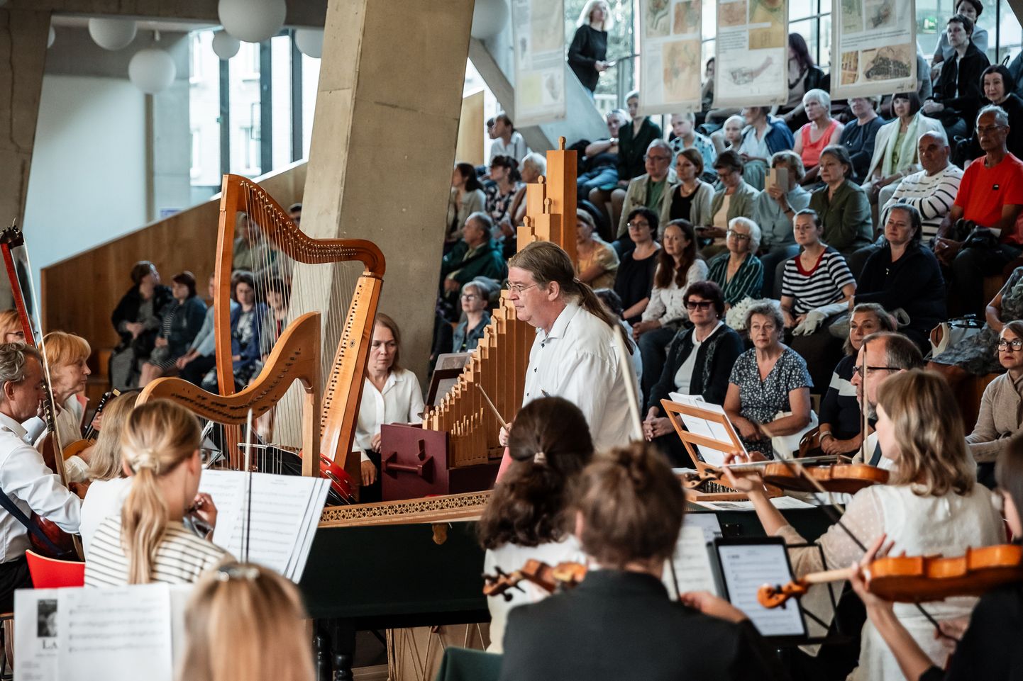 Таллиннский барочный оркестр под управлением капельмейстера Эндрю Лоуренса-Кинга выступает в фойе Нарвского колледжа, заполненном публикой.
