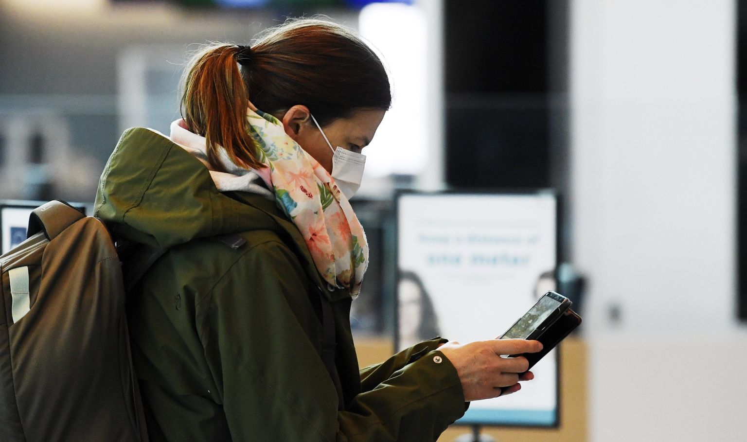 A passenger, wearing a face mask, looks at her phone at the Helsinki International Airport in Vantaa.