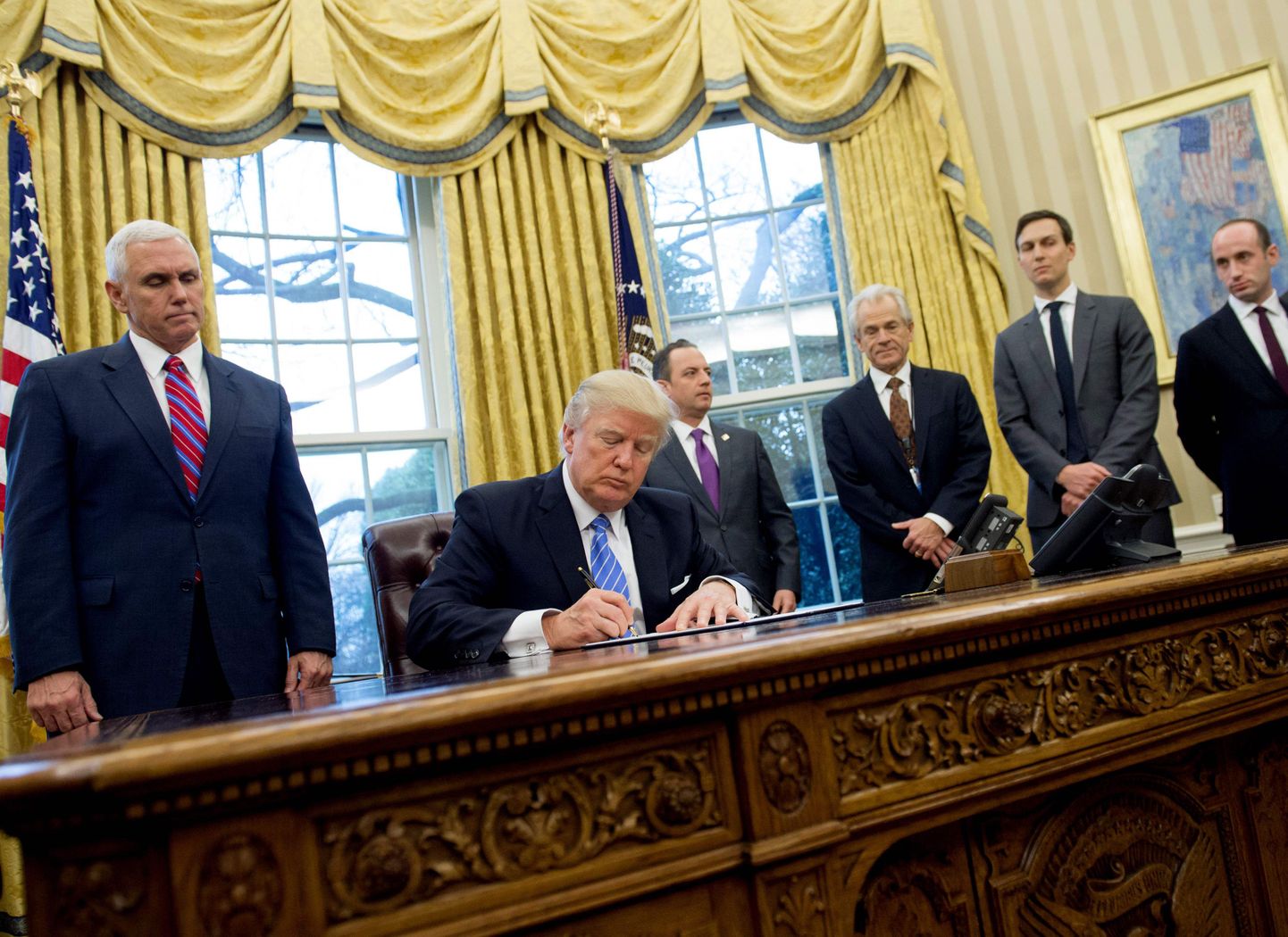Vasakul seisab asepresident Mike Pence, kes vaatab, kuidas president Donald Trump allkirjastab ühte oma esimestest dokumentidest.