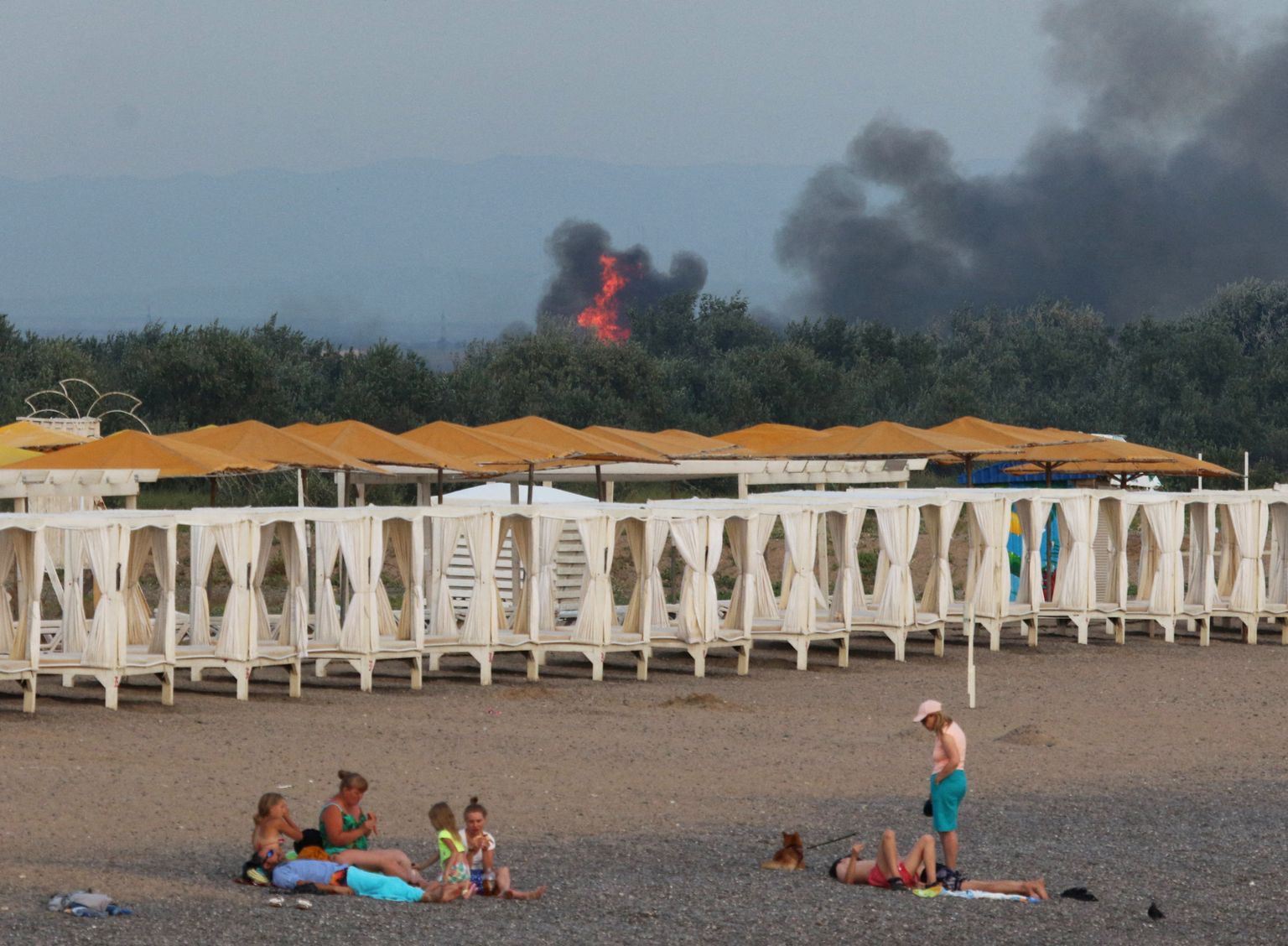 Отдыхающие на пляже в Крыму на фоне взрывов на российской военной авиабазе в Новофедоровке, 9 августа 2022 года.