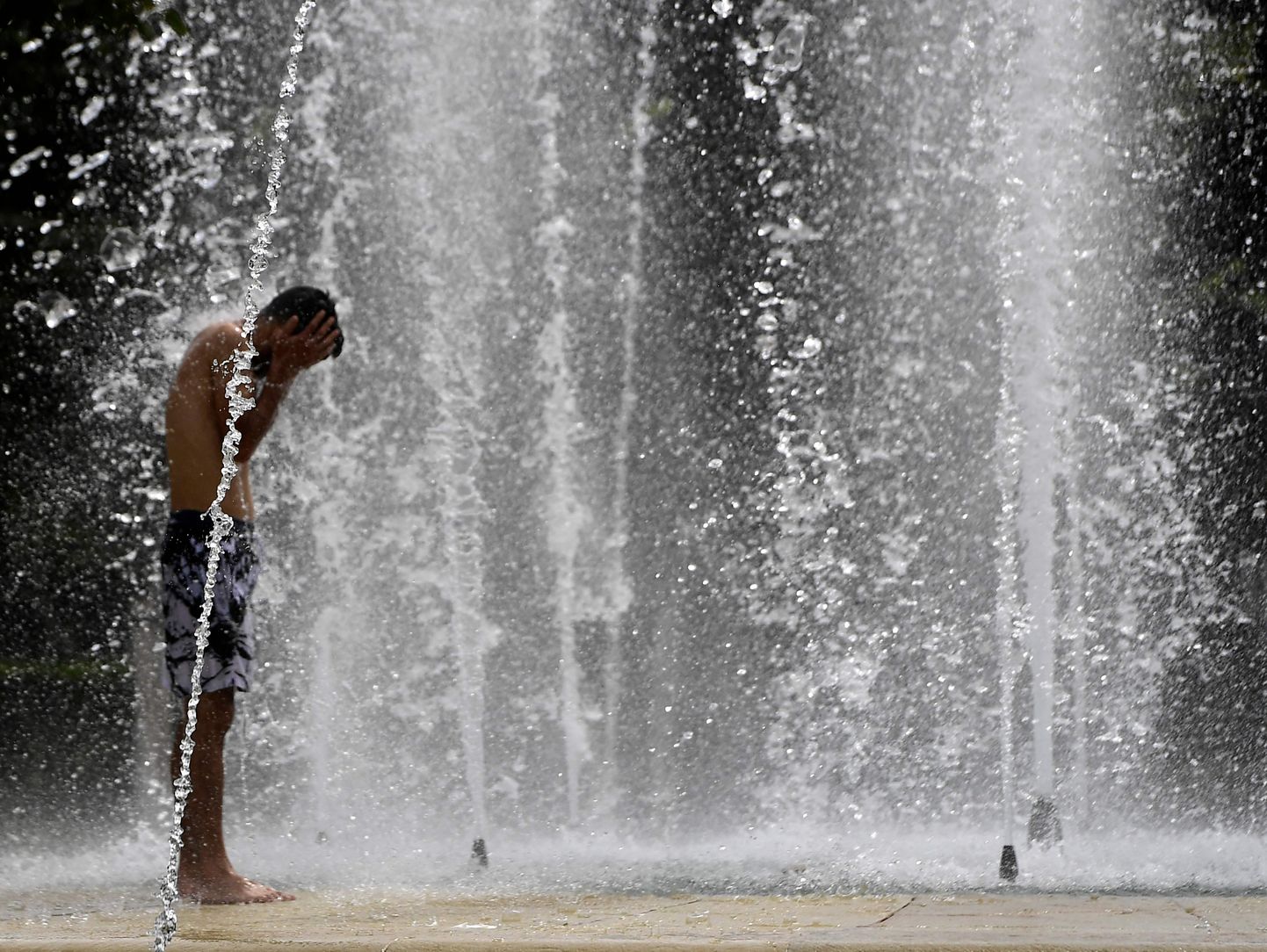Мужчина в Севилье охлаждается в фонтане.