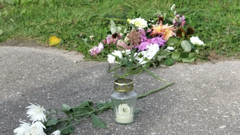 Ziedi un svece uz taciņas, kas atrodas blakām vietai, kur tika atrasta noslepkavotā desmitgadīgā Diāna Kozlovska