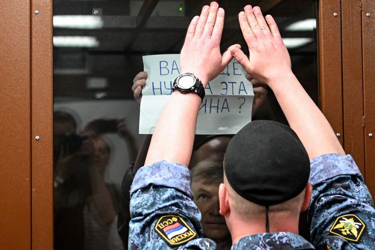 Алексей Горинов пытается показать из клетки в зале суда самодельный плакат "Вам ещё нужна эта война?"