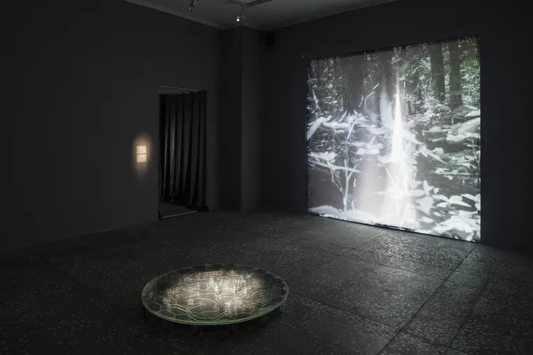 Esiplaanil «Kaev/Well». Graveeritud peegel, klaas, 2022. Taustal «Rituaal/The Ritual». HD video, 2022.