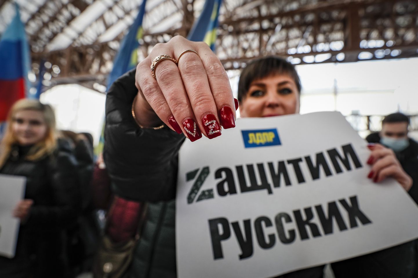 Vene naine hoidmas plakatit, millele on kirjutatud "Kaitskem venelasi". Samuti on naise küünel näha V- ja Z-tähti – sümboolikaid, mida kasutab Ukraina vastu sõdiv Vene sõjavägi.