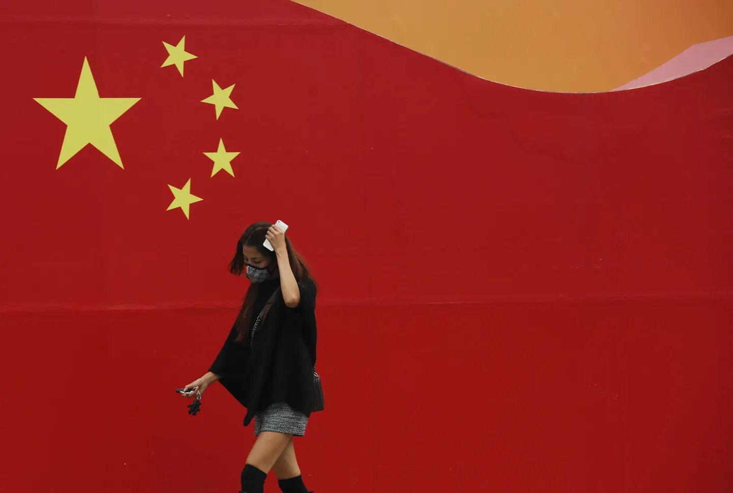 Maskiga naine möödub seinale maalitud Hiina lipust Pekingis.