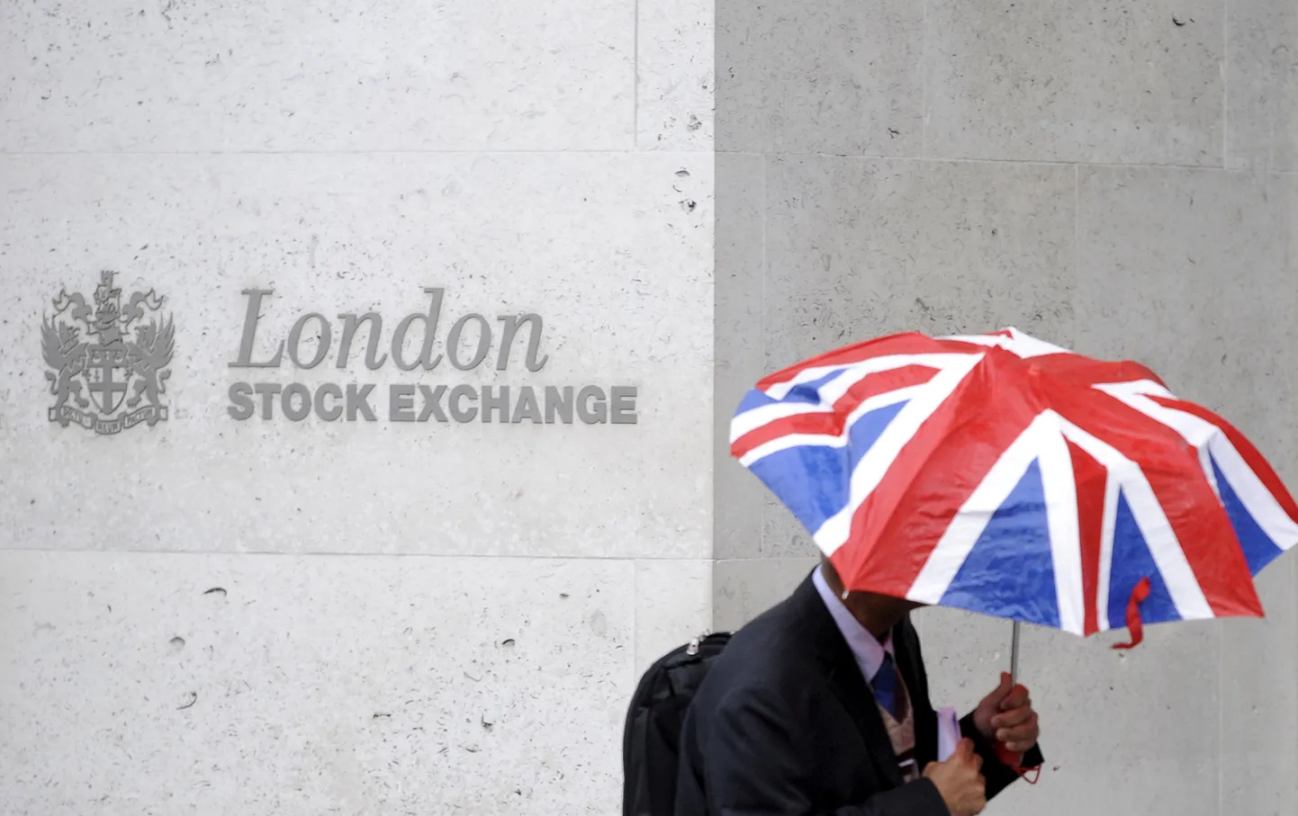A worker shelters from the rain under a Union Flag umbrella as he passes the London Stock Exchange in London, Britain, October 1, 2008.  REUTERS/Toby Melville/File Photo