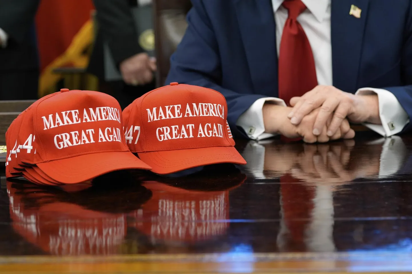 USA president Donald Trump istub Valge Maja ovaalkabinetis, tema ees laual nokamütsid kirjaga «​Make America Great Again»​ehk «Teeme Ameerika taas suureks».